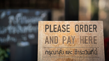 "Order and pay here" wooden banner (in English and Thai langauge) that placed on the counter of cafe and restaurant. Sign for business place object photo. Close-up.