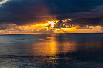 Sublime sunset piercing the clouds above the sea in Okinawa beach, Japan. Calm sea reflections, beautiful twilight and dramatic sky in horizontal image