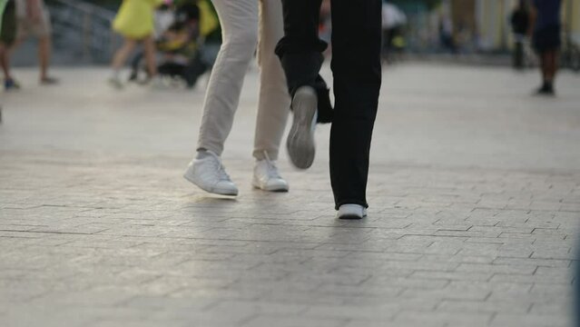 Legs of two people in dancing motion on city sidewalk, highlighting the rhythm and flow of their movement