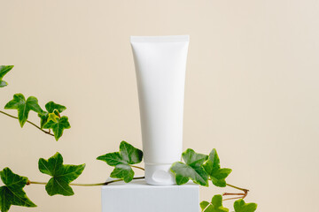 Facial care cream with green plant leaves on podium at beige background. Natural organic skincare, body lotion, face cream. Mockup cream bottle for beauty products, aesthetic minimal style
