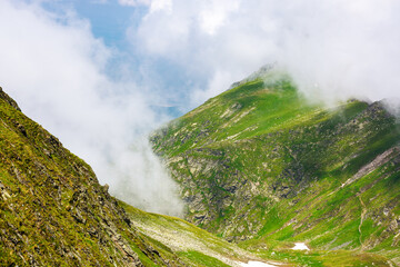 green hillsides of fagaras ridge in summer. clouds among the slopes. beautiful mountainous landscape of romania on a sunny day
