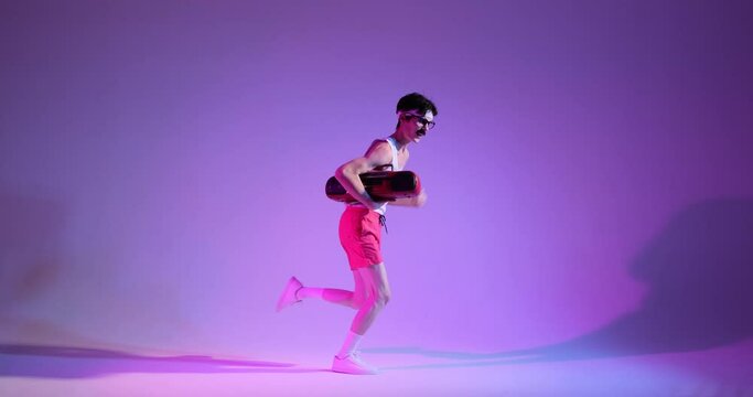 Retro freaky Caucasian 90s man dancing and running on purple background, holding ghettoblaster in hands. Enjoying music, entertainment concept.
