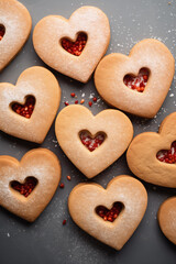 A group of romantic hollow heart-shaped cookies decorated with powdered sugar and red berries. A close-up flat lay of sweet treats arranged on a table for Valentines day. AI-generated