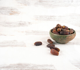 Antique earthenware bowl full of dried date fruits. Old painted white wooden background copy space. Ramadan  concept  heap of palm tree fruits.