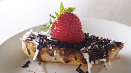 grilled bananas adorned with a delectable ensemble of chocolate, grated cheese, and fresh strawberries, elegantly presented on a plate a top a rustic wooden table.