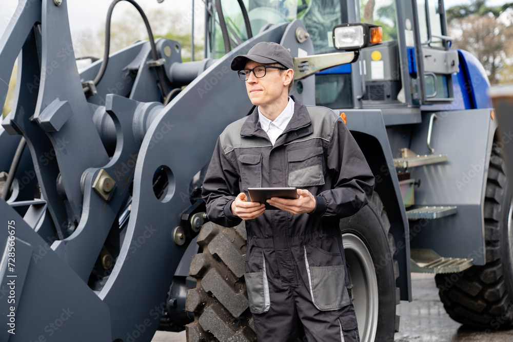 Poster serviceman with digital tablet on a background of the tractor.