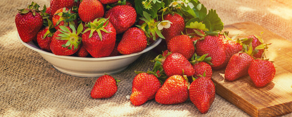 Strawberries on a white plate and a wooden cutting board on the table. Horizontal banner