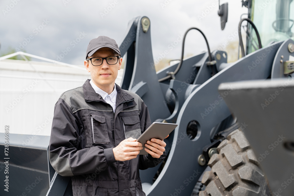 Poster serviceman with digital tablet on a background of the tractor.