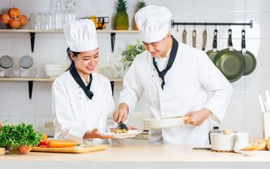 Two Asian professional couple chef wearing white uniform and hat, helping for preparing ingredients...