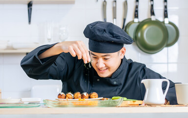 Portrait close up handsome professional Japanese male chef wearing black uniform, hat, cooking, making takoyaki street food, smiling with confidence, standing in kitchen. Restaurant, Hotel Concept.