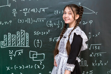 Teenage girl near the school board, portrait of a student 12-14 years old. White apron of schoolgirl graduate
