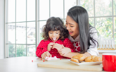 Beautiful Asian woman wearing apron and little cute daughter girl, smiling with happiness, having...