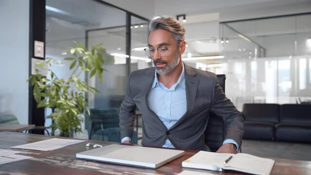 Mature European Latin business man ceo trader come to office and start a new working day, using computer, typing, working, doing online data market analysis, thinking planning tech strategy at laptop.