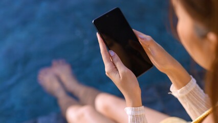 close up asian female hand using smartphone relax casual summer vacation pool side sunset moment,...