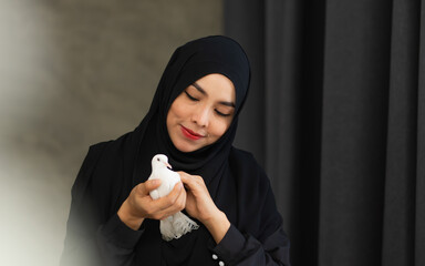 Portrait with copy space adult beautiful Muslim woman wearing black headscarf, traditional dress, smiling with happiness, holding white bird, showing freedom, beauty. Diversity, Woman Power Concept.