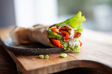 Tortilla wrap with fresh vegatables and fried chicken meat on a plate. Background concept with for...