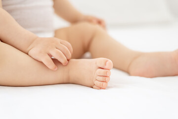 close-up of legs and arms of a small child a girl or a boy in a white bodice on the bed in the nursery