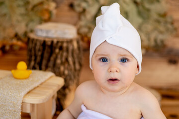 a cute little child in a towel and a turban on his head after bathing sits in a steam room in a...
