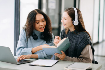 Two Attractive young female college students working on the school project using computer and tablet together, enjoy talking and headphones having a video chat.