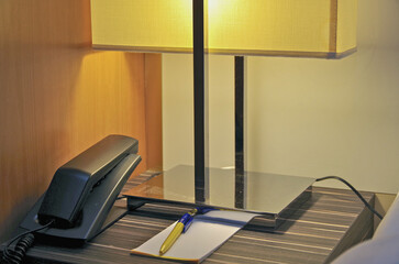 Night stand lamp with telephone and notepad with pen inside cabin stateroom onboard modern luxury...