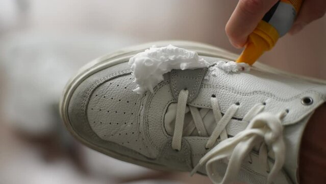 Close-up hands of unrecognizable man applying cleaning foam to dirty white sneakers. Process cleaning white canvas sneakers from dirt and dust. Concept of caring for leather footwear, slow motion.