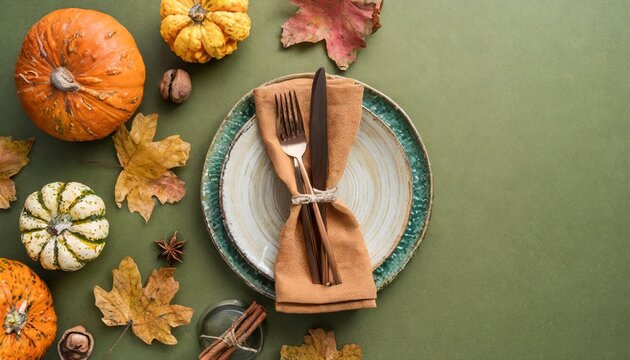autumnal table decor idea top view vertical shot of plate cutlery napkin tablecloth glass cinnamon sticks pumpkins autumn leaves on olive background with empty space for advert or text