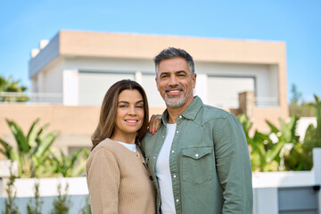 Happy smiling mature older family couple new property buyers modern villa owners standing outside...