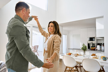 Romantic happy older mature couple in love dancing at home kitchen. Affectionate middle aged senior man and woman in love standing in modern cozy house enjoying dance. Authentic candid photo.
