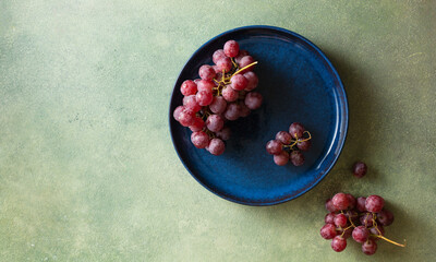 Red grapes on a dark blue plate. Food background with space for text. Autumn concept.
