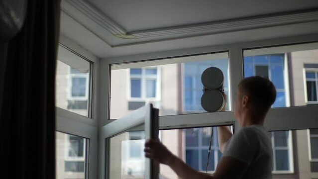 Rear view of unrecognizable man launched automatic robot for washing windows in apartment. Intelligent home appliance for washing hard-to-reach windows. Concept of cleaning house with smart devices.