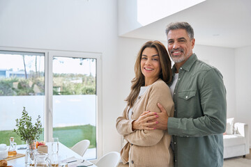 Portrait of happy smiling mature older family couple real estate owners standing at home, affectionate senior middle aged man and woman in love hugging in modern house house living room interior. - Powered by Adobe