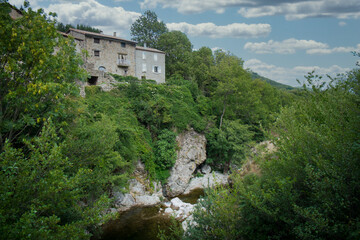 Fototapeta na wymiar This image encapsulates the serene and timeless beauty of the Ardeche region, with a traditional stone house perched atop a rocky outcrop, surrounded by verdant flora. The flowing river below and the
