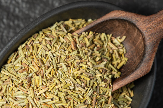 Close-up of dry chopped rosemary in a bowl with a wooden scoop. Top view.