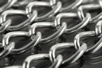 Close-up of metal chains stacked in a row on a reflective surface.