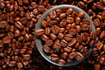Fototapeta premium A bowl of roasted coffee beans in a pile of coffee beans. Top view. Studio shot.
