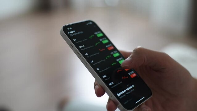 Closeup side view of stock trader holding using smartphone analyzing financial data on stock market price. Close-up of male investor check online trading platform application, buy cryptocurrency.
