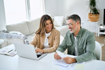 Happy middle aged couple older man and woman calculating investments and financial expenses, money...