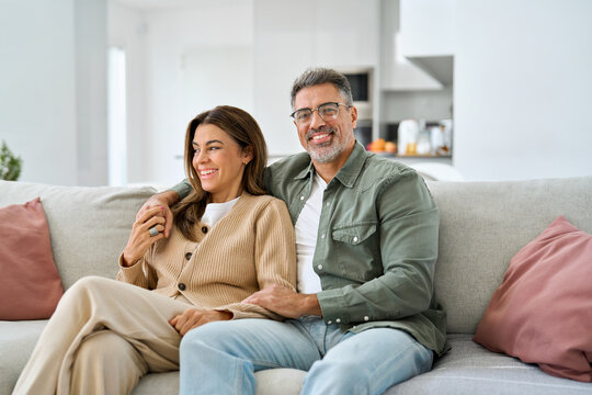 Happy middle aged mature romantic couple in their 40s hugging sitting on couch at home. Smiling older man and woman in love relaxing on sofa together enjoying chilling in modern house living room. - Powered by Adobe