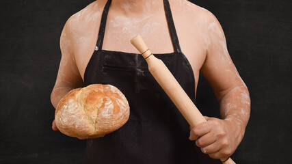 Torso of a male chef in an apron and bread in his hand on a black background.