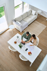 Middle aged man and woman using laptop computer sitting at table in living room interior. Mature...