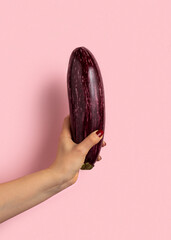 Woman's hand holds eggplant on pink background.