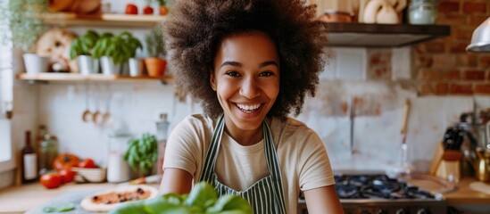 Biracial girl with afro hair watching cooking classes, learning pizza making from video blog in modern kitchen, smiling with basil leaf.