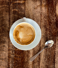 Coffee cappuccino in the white cup on the wooden background. Top view. Close-up.