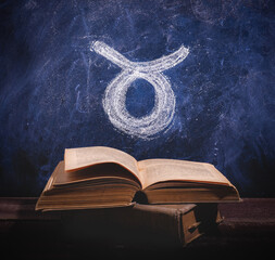 Zodiac sign Taurus on a chalkboard above old astrology books.