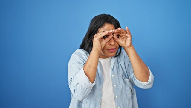 A joyful middle-aged hispanic woman gestures with her hands in front of a blue isolated background, expressing playfulness and happiness.