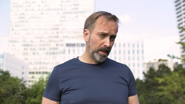 A handsome middle-aged Caucasian man shakes his head and shows a thumb down to the camera in a park