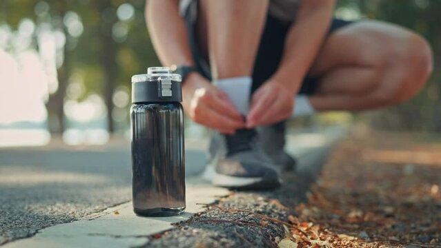 Closeup on black bottle of water, Blurred man tie their shoes before run or jogging on track race in the public park, Healthy