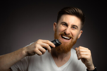 Handsome bearded man cutting his own hair with a clipper
