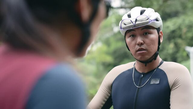 two young asian cyclist having a discussion at roadside while taking a break from outdoor riding