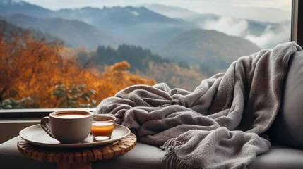 Abwaschbare Fototapete Wide panoramic closeup background banner photo, view from a luxury hotel bedroom window, cozy couch with pillows and coffee cup on a tray, misty mountain range landscape outside in a cold day morning © Sudarshana